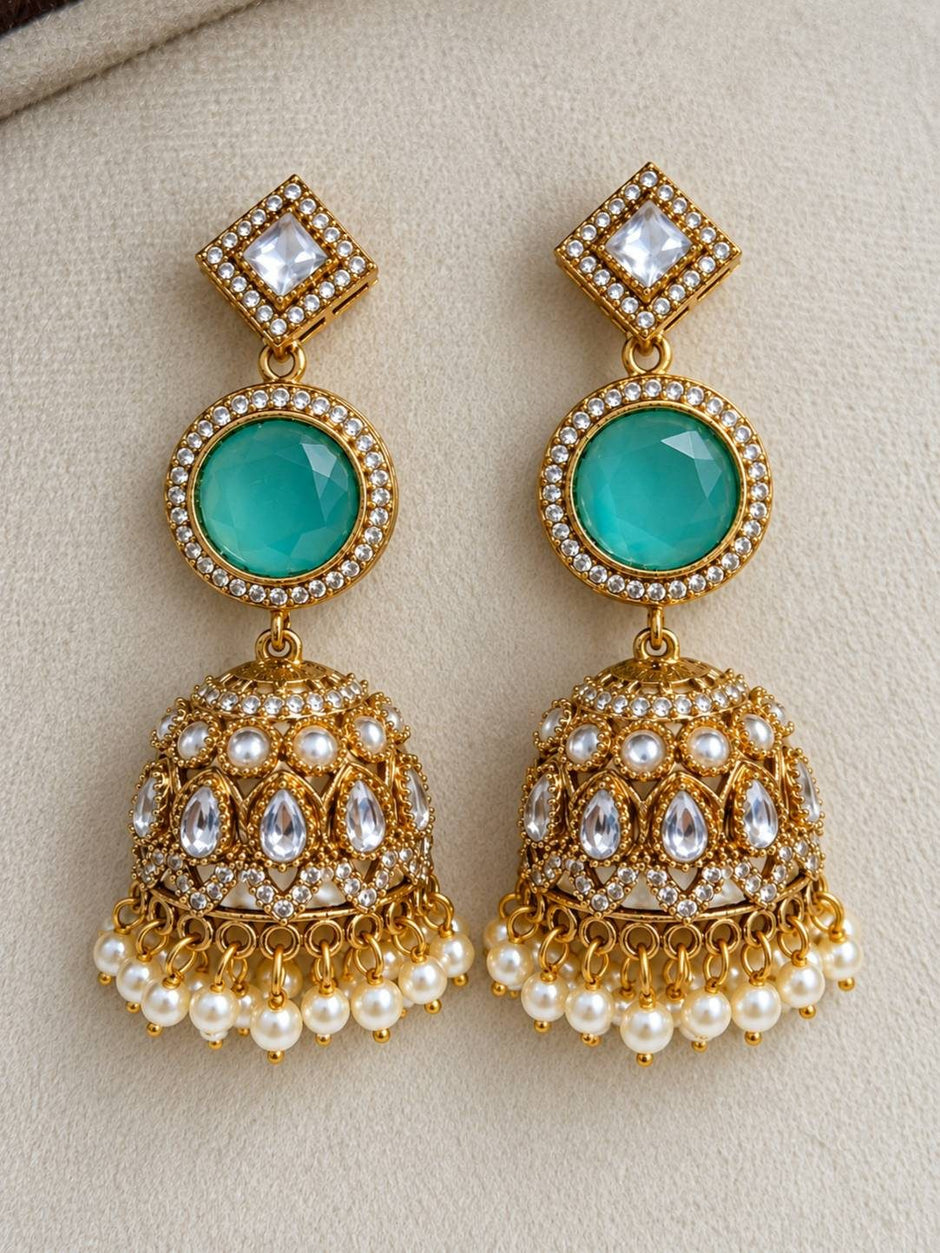 Pair of gold-plated kundan jhumka earrings with turquoise stones, polki settings and pearl drop fringe on beige surface