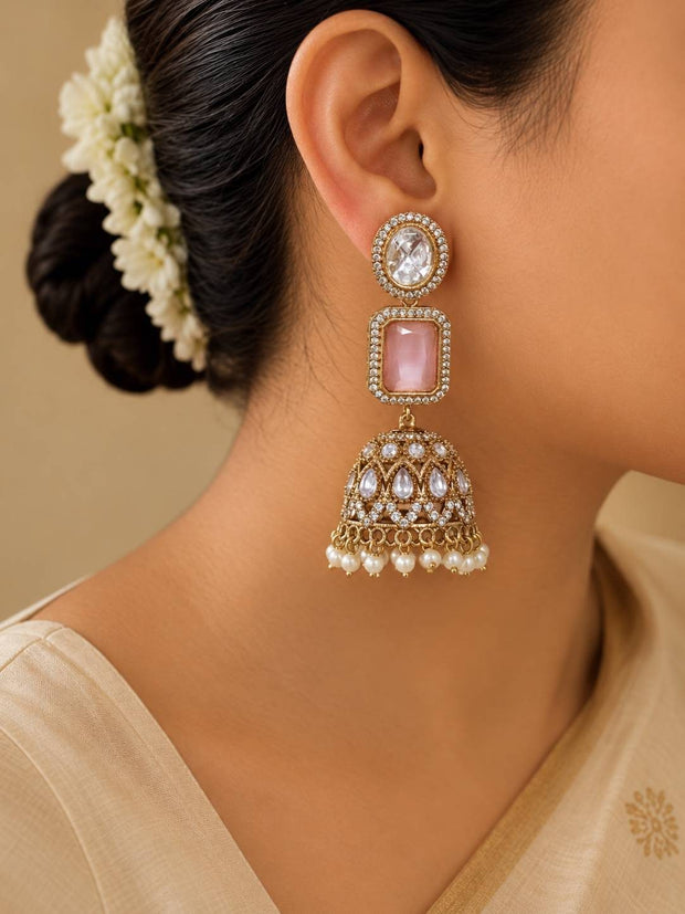 Woman wearing gold-plated kundan jhumka earring with pink stone and pearl drops, styled with white floral hair accessory and cream outfit