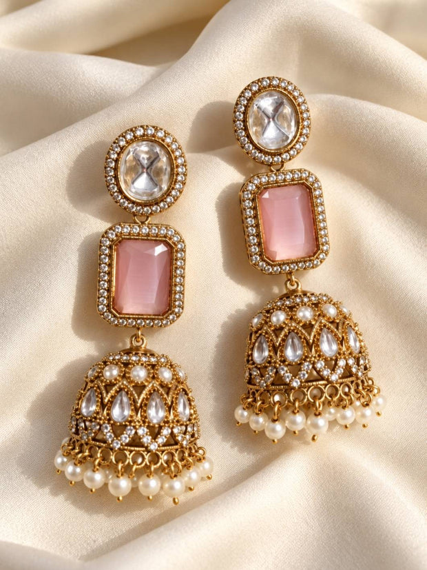 Pair of gold-plated kundan jhumka earrings with pink rectangular stone and pearl drop fringe laid on cream silk fabric