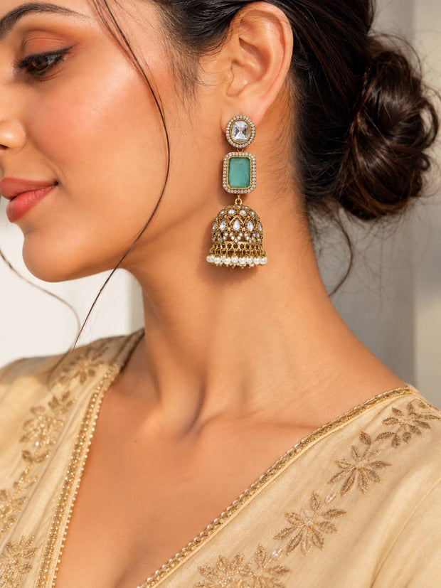 Woman wearing gold-plated mint stone kundan jhumka earring with cream embroidered saree, side profile