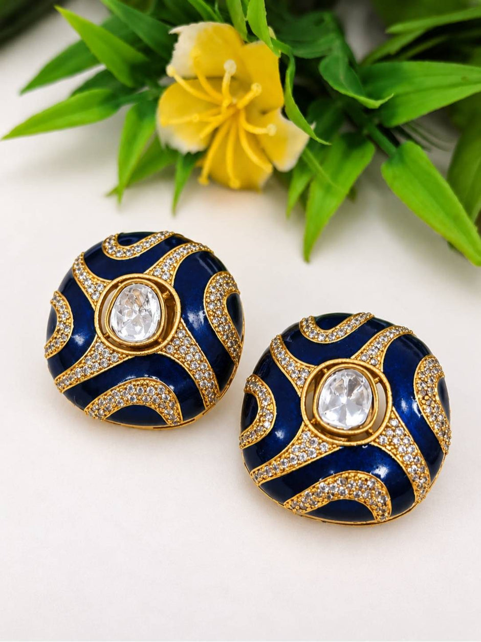 Pair of navy blue enamel kundan dome stud earrings with gold-toned ridges and oval centre stone, placed on white surface beside yellow flower