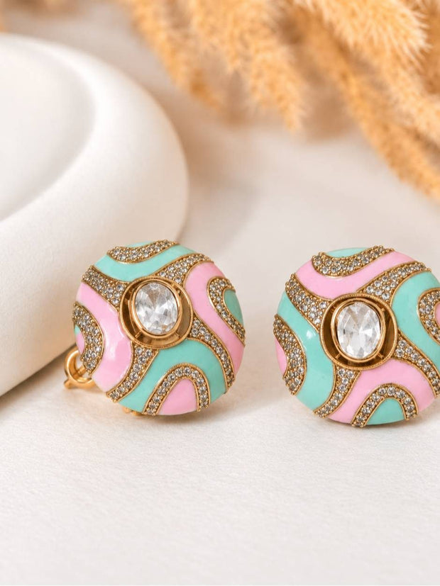 Close-up of two gold-toned enamel dome studs with swirling mint and blush pink enamel and micro-crystal detailing, displayed on a white prop