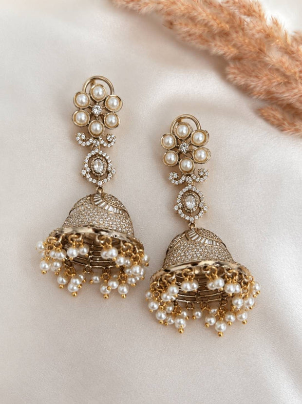 Pair of gold-plated pearl jhumka earrings laid flat on ivory silk fabric with dried pampas grass
