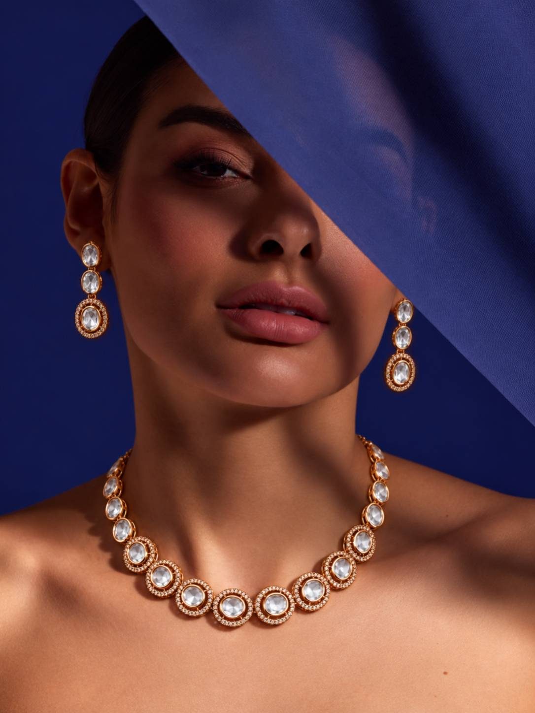 Model wearing rose gold kundan necklace set against a blue draped fabric background