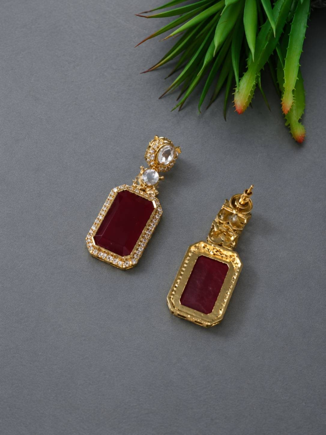 Pair of gold-plated kundan ruby rectangular drop earrings showing front and back sides on grey surface