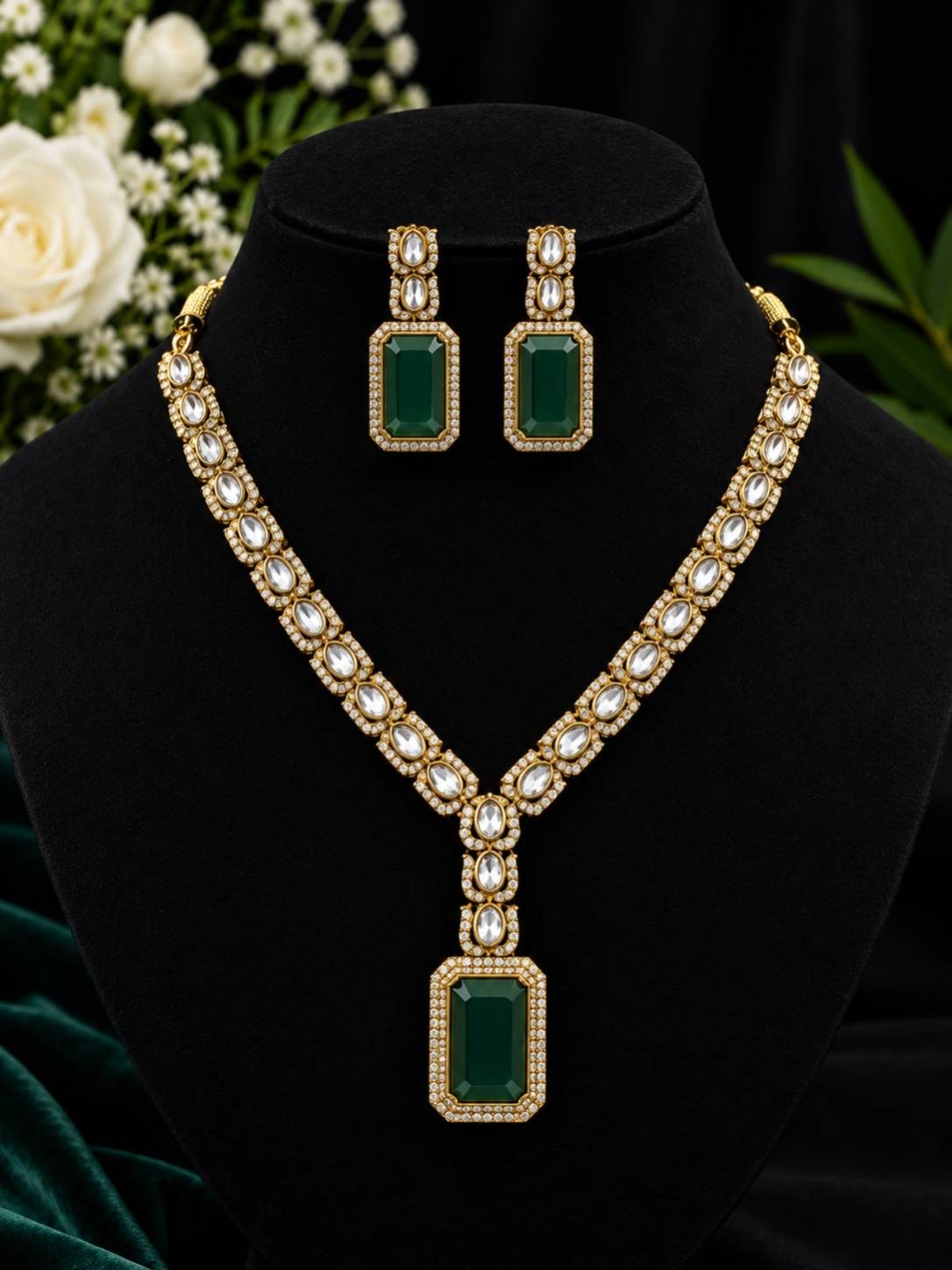 Gold-plated kundan necklace set with emerald green rectangular pendant and matching drop earrings displayed on black jewellery bust