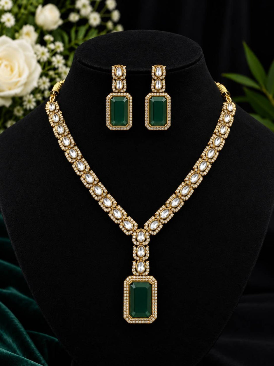 Gold-plated kundan necklace set with emerald green rectangular pendant and matching drop earrings displayed on black jewellery bust