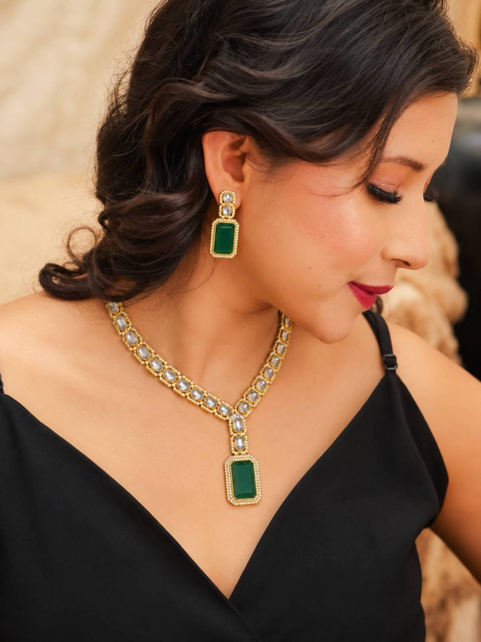 Woman wearing gold-plated kundan necklace with emerald green pendant and matching earrings over a black outfit