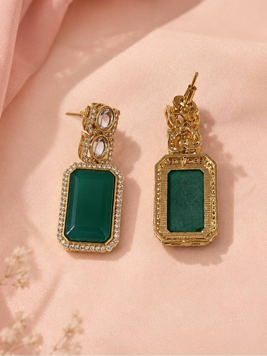 Front and back view of emerald green rectangular drop earrings with kundan top and gold-plated halo frame on peach fabric
