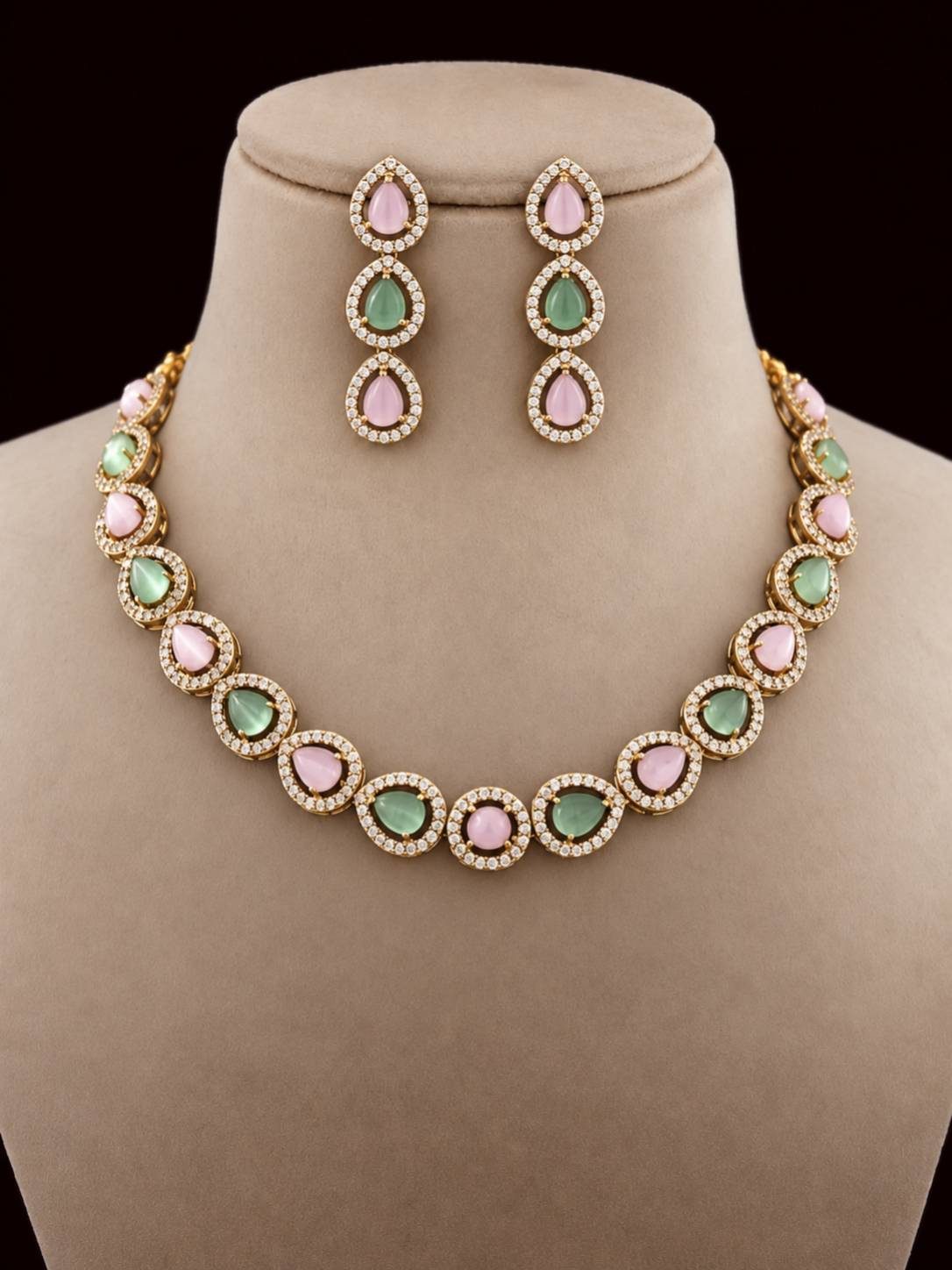 Gold-plated choker necklace and drop earrings with pink and green cabochon stones displayed on a beige jewellery bust