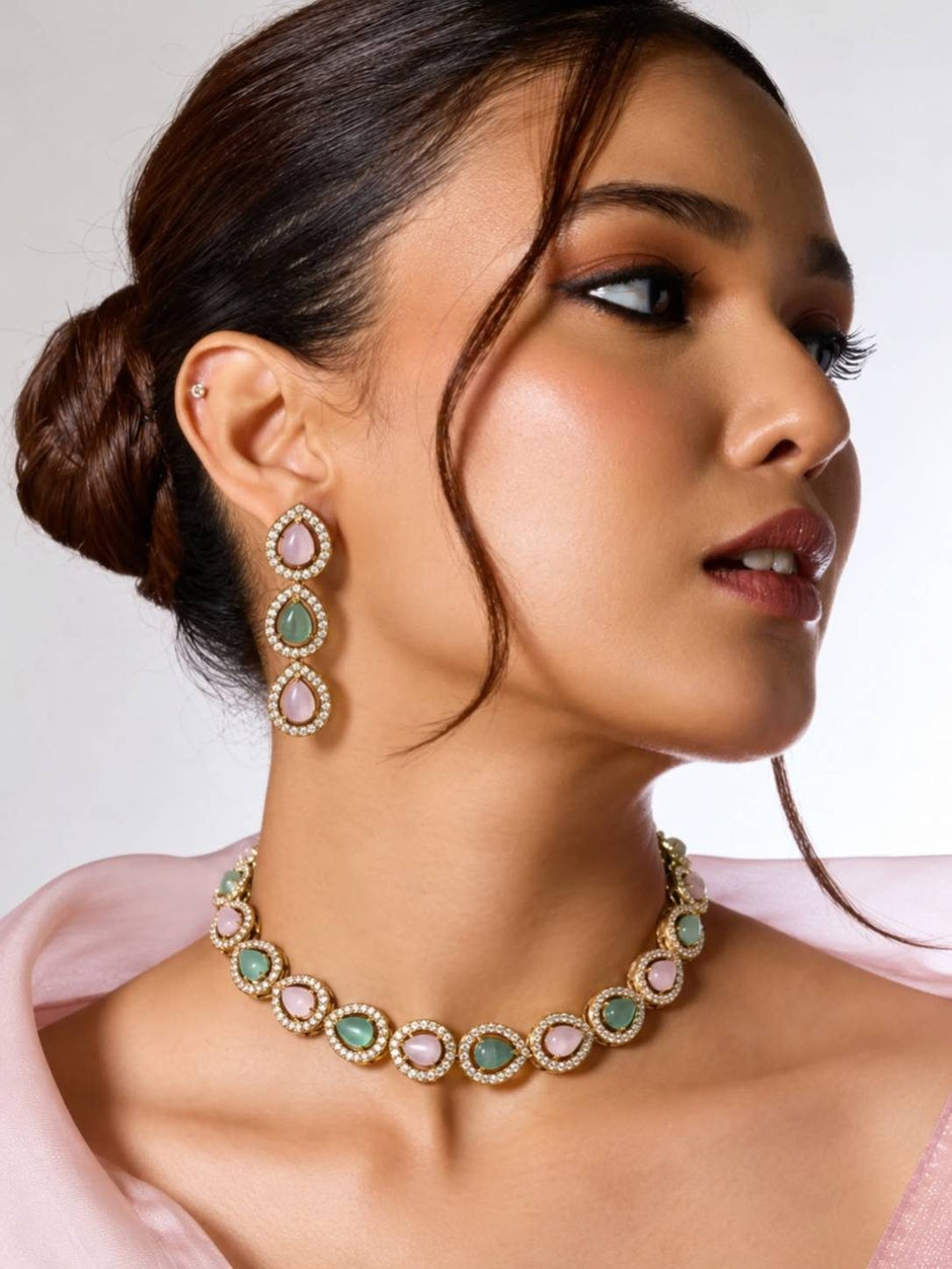Woman wearing pink and green stone gold-plated choker necklace and three-tier drop earrings with a blush pink outfit