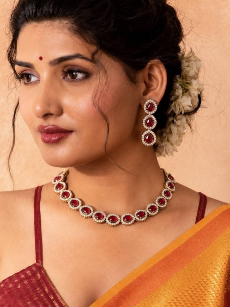 Woman wearing gold-plated ruby CZ choker necklace and drop earrings with a red and orange silk saree and white flowers in hair