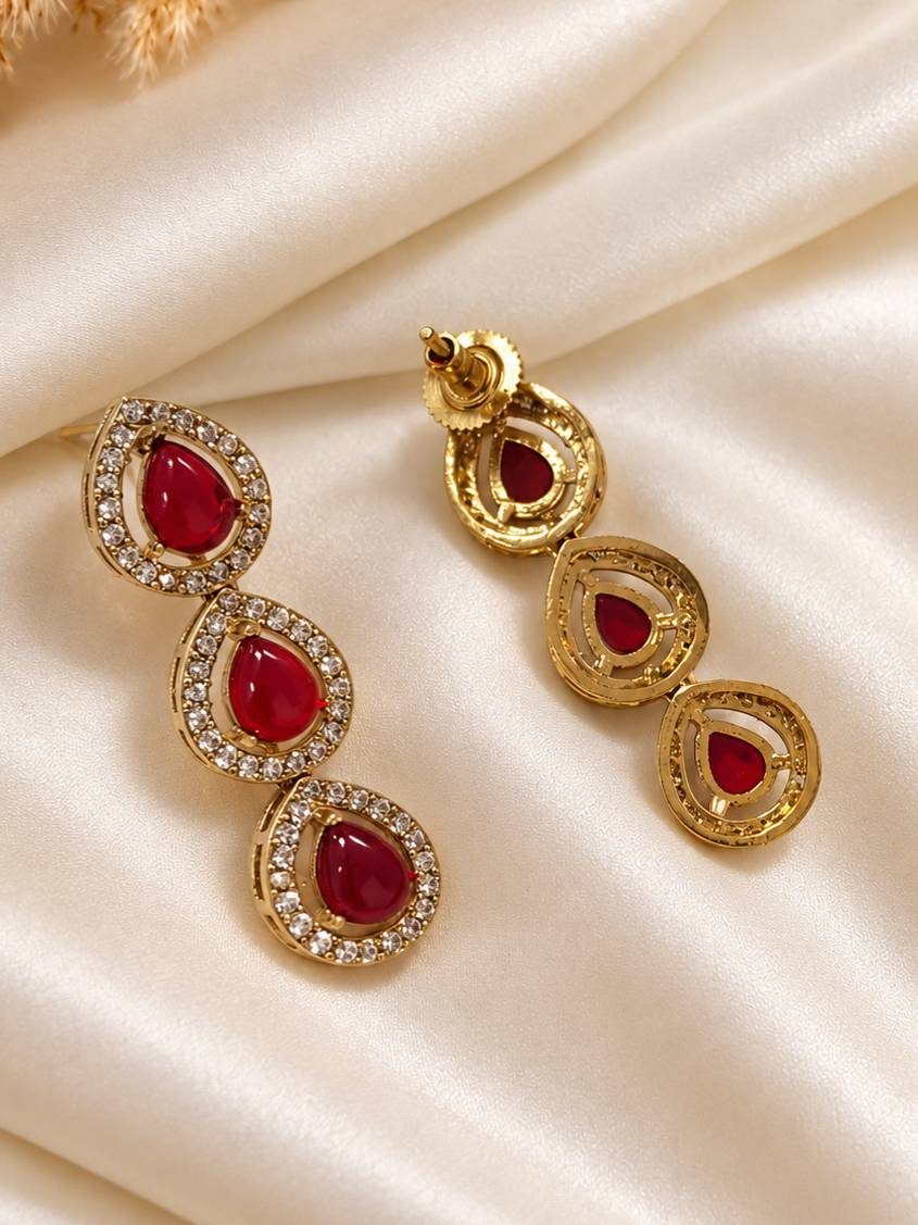 Front and back view of gold-plated triple teardrop ruby CZ drop earrings laid flat on ivory satin fabric