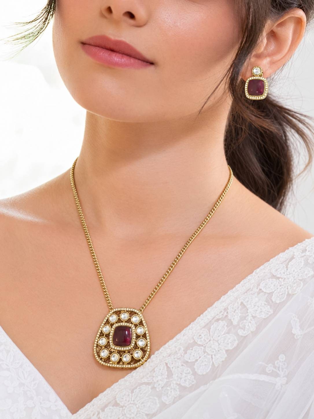 Model wearing gold-plated red cabochon kundan pendant necklace and matching stud earrings with a white embroidered off-shoulder top