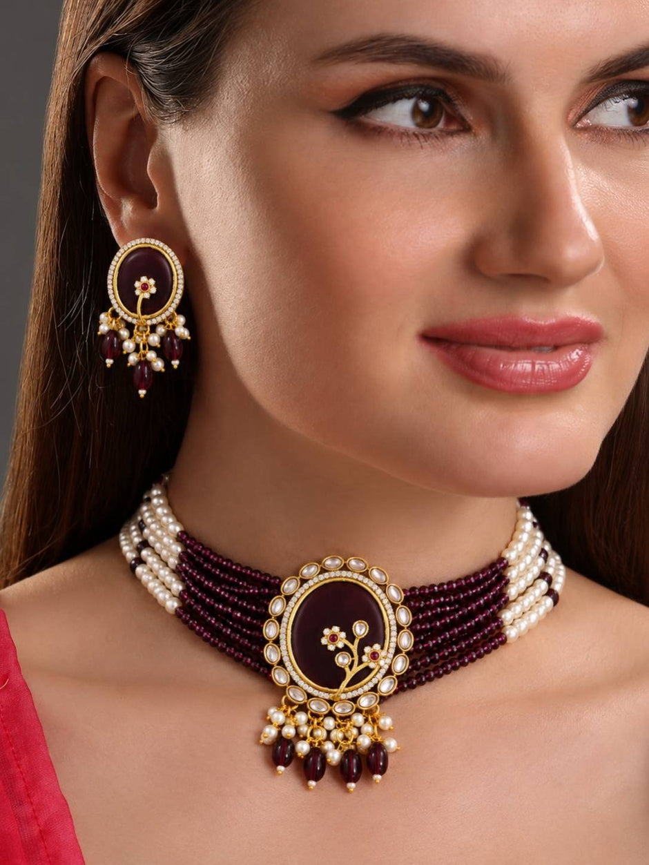 Woman wearing wine kundan choker necklace and matching oval stud earrings with a pink outfit