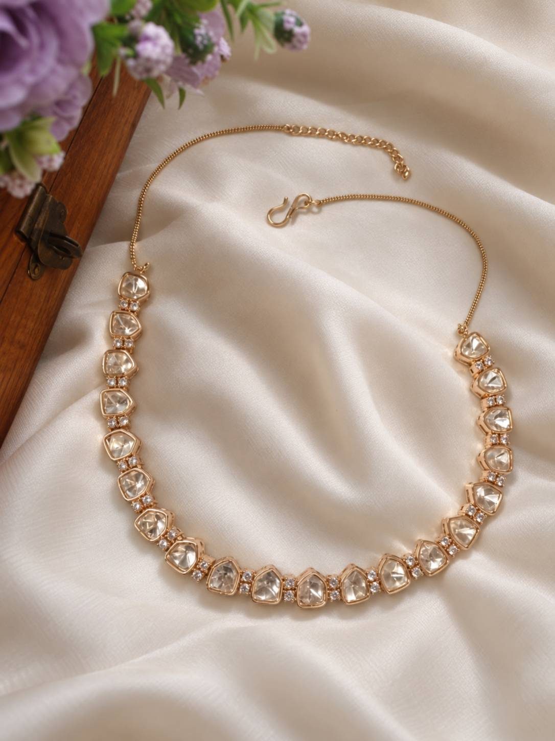 Rose gold polki choker necklace laid flat on ivory silk fabric with an adjustable chain clasp visible