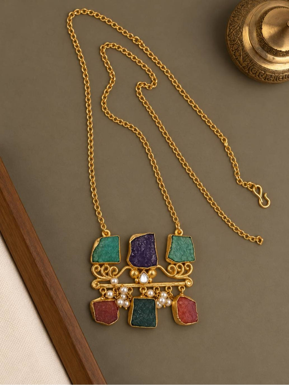 Flat lay of gold-plated raw stone pendant necklace with long rolo chain on grey surface