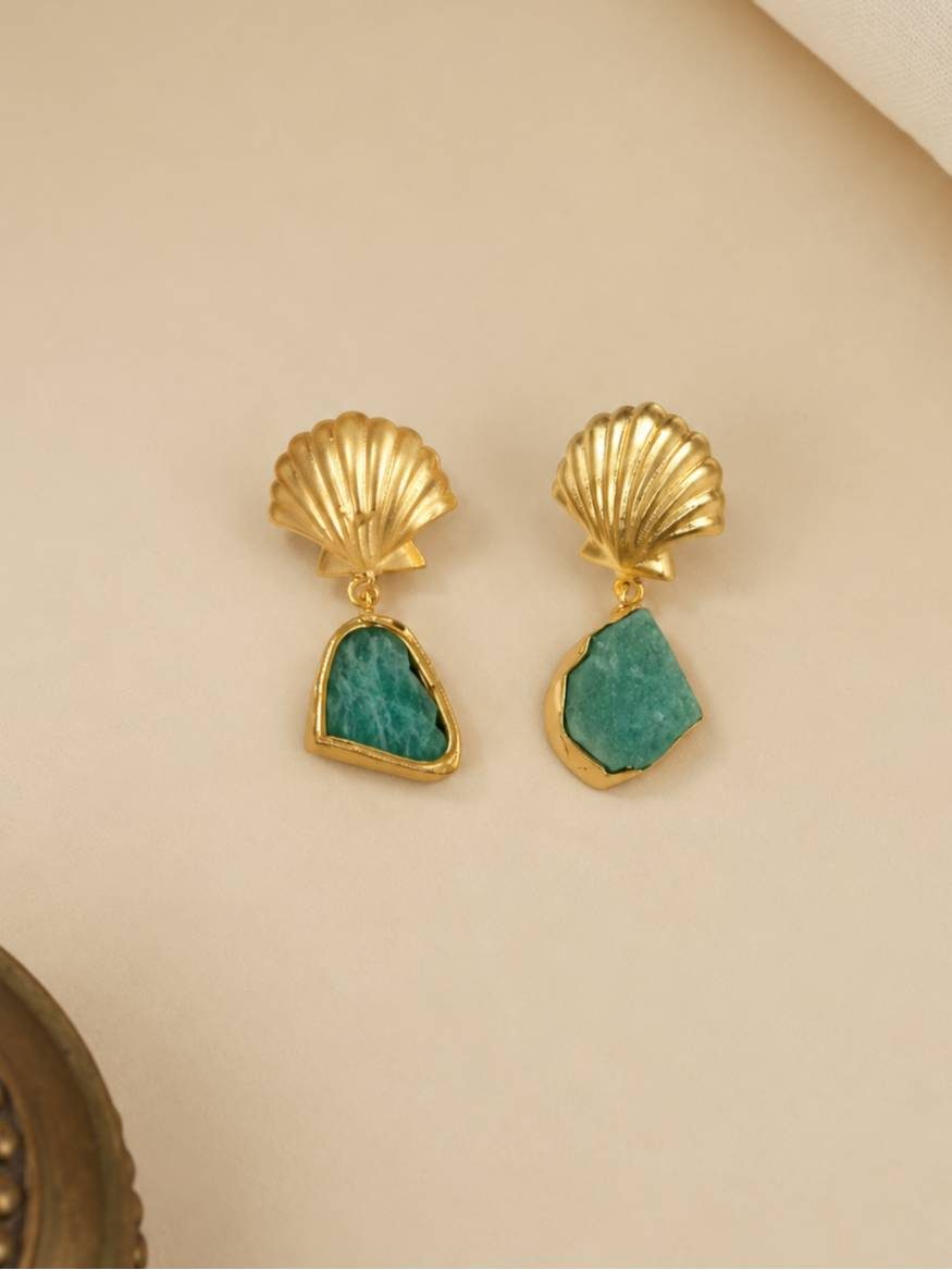 Close-up of gold seashell stud earrings with rough freeform green amazonite drops on a cream background