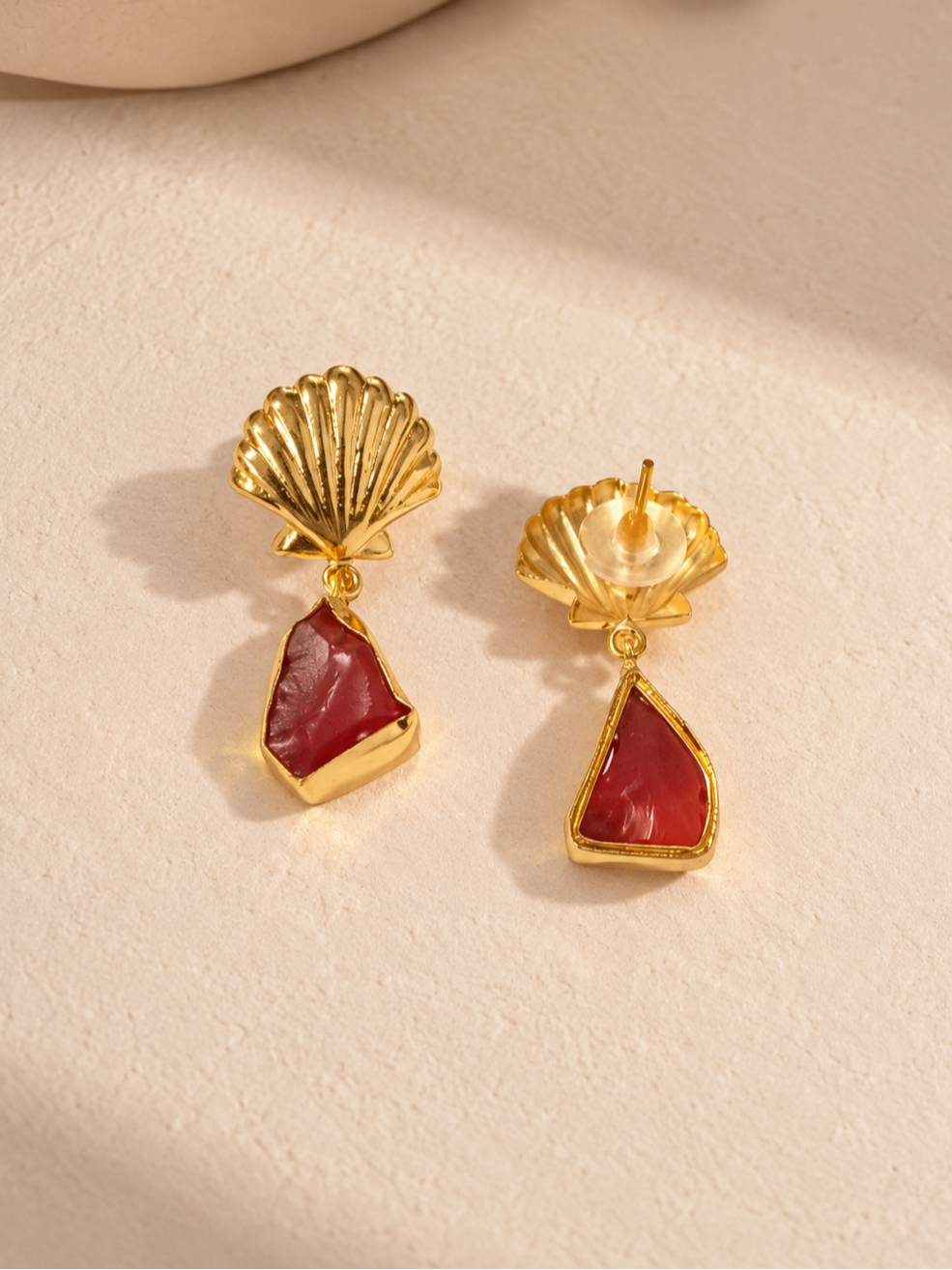 Close-up of gold scallop shell stud earrings with rough red stone drop, front and back view