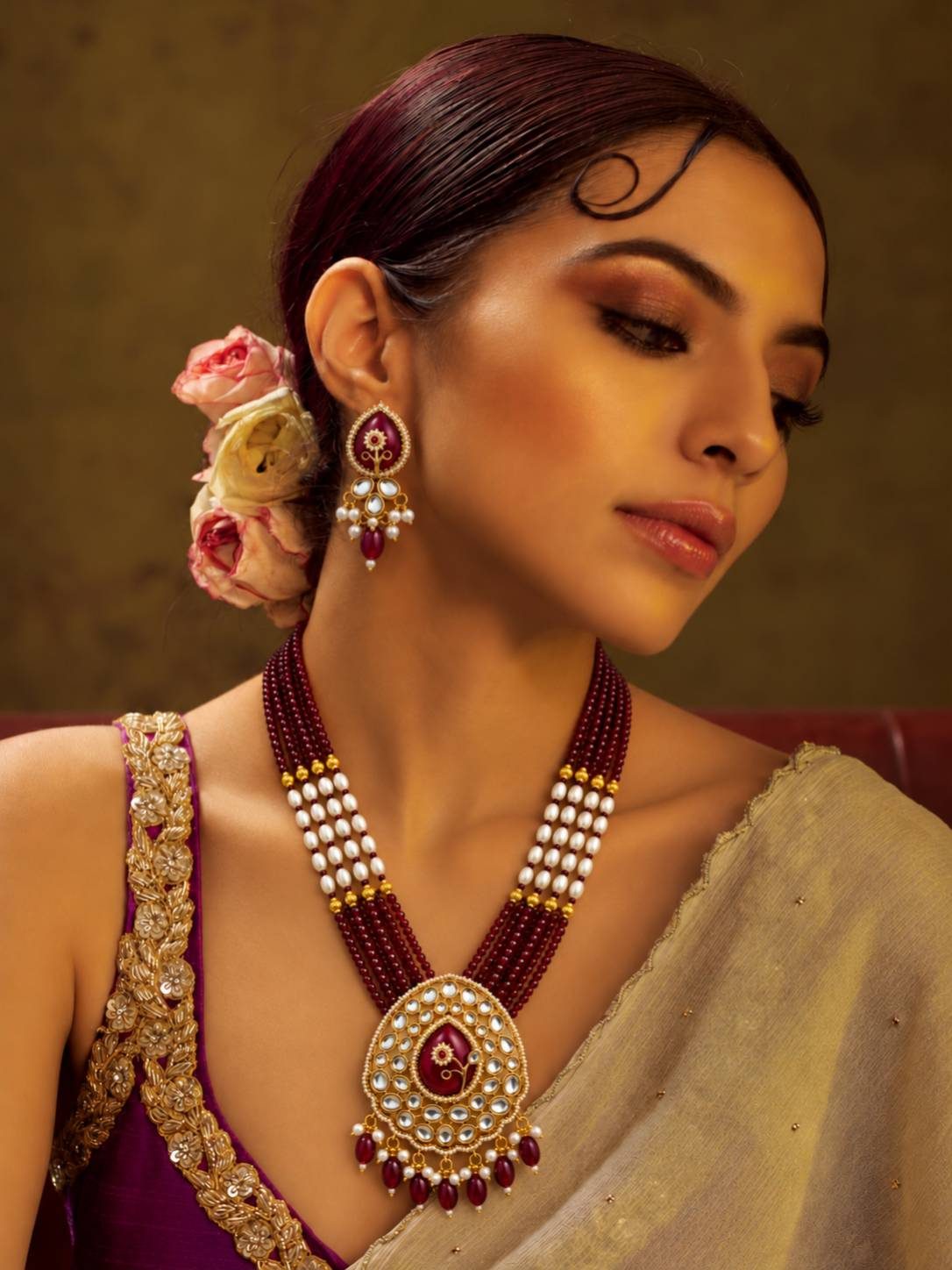 Model wearing ruby kundan long necklace set with pearl beads over a magenta embroidered saree blouse with flowers in hair