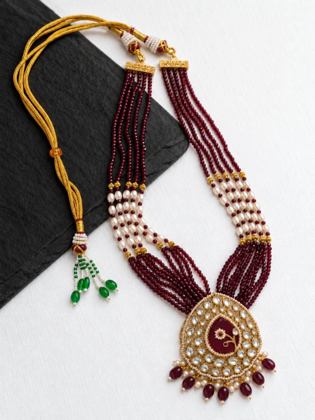 Full-length view of ruby beaded kundan necklace laid flat on slate surface showing gold dori closure and green tassel detail