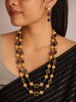 Woman wearing gold-plated layered beaded necklace and matching earrings styled with a black striped saree