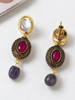 Close-up of matching drop earrings showing frosted oval top, antique-framed ruby-tone cabochon centre, and blue bead drop