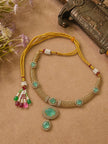 Gold-plated green stone necklace with adjustable yellow dori tie-back and colourful tassel laid flat on a beige surface