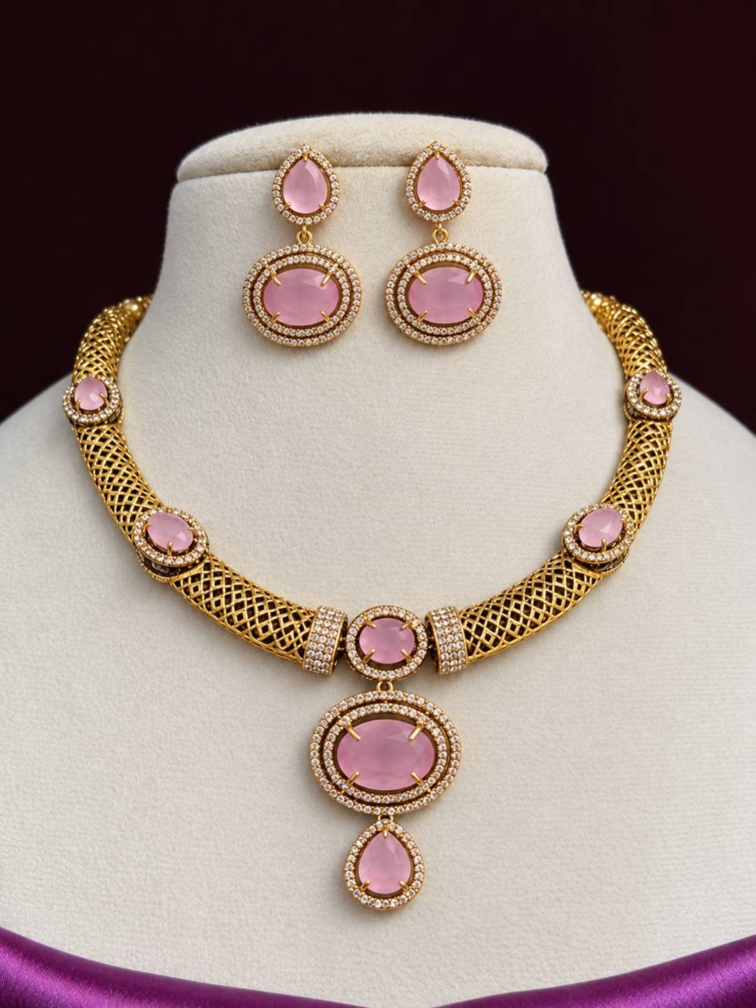 Gold-plated pink stone choker necklace and drop earring set displayed on a jewellery bust