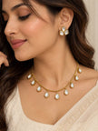 Woman wearing gold-plated kundan drop necklace and matching three-stone stud earrings with a cream saree