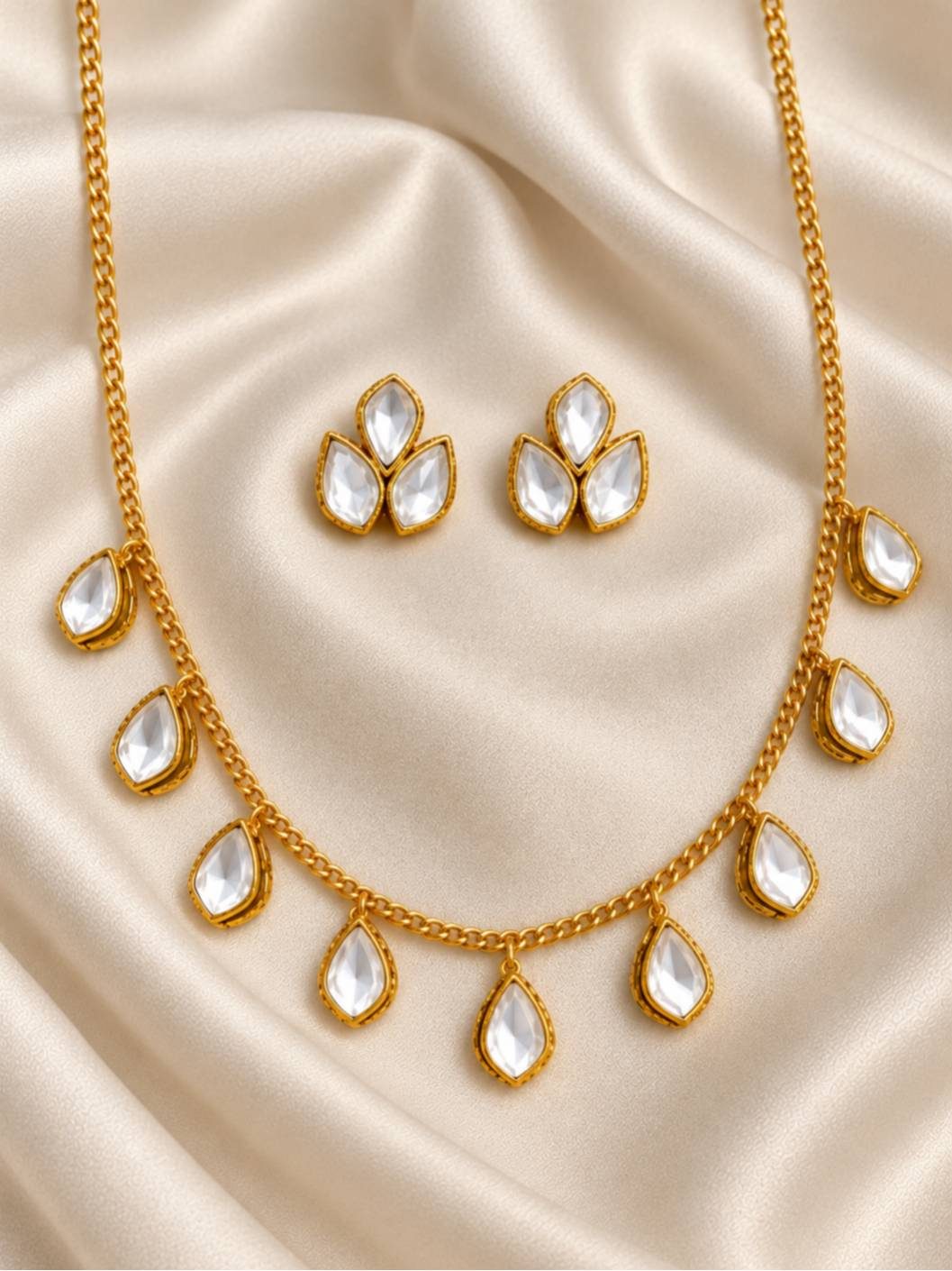 Kundan drop necklace and stud earrings laid flat on ivory silk fabric, showing full set detail