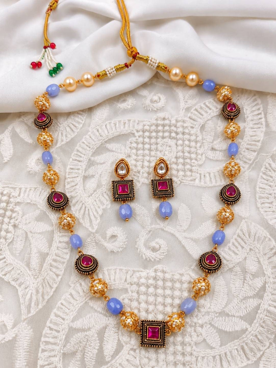 Gold-plated beaded mala necklace and earrings laid flat on white embroidered fabric