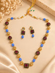 Gold-plated kundan beaded necklace set with blue barrel beads and matching drop earrings laid flat on cream fabric with dried flowers