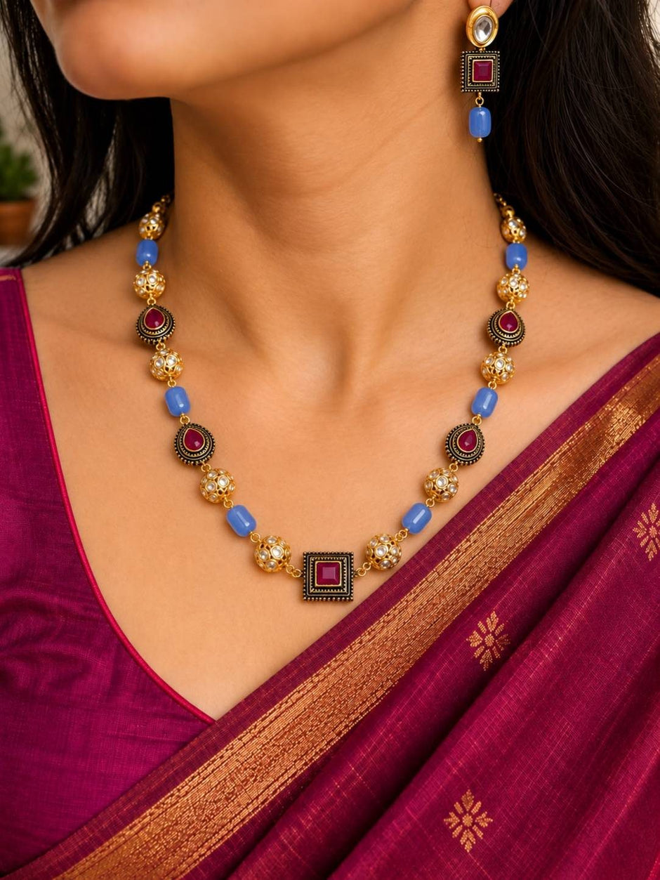 Woman wearing gold-plated kundan beaded necklace and matching earrings with a deep magenta silk saree with gold border
