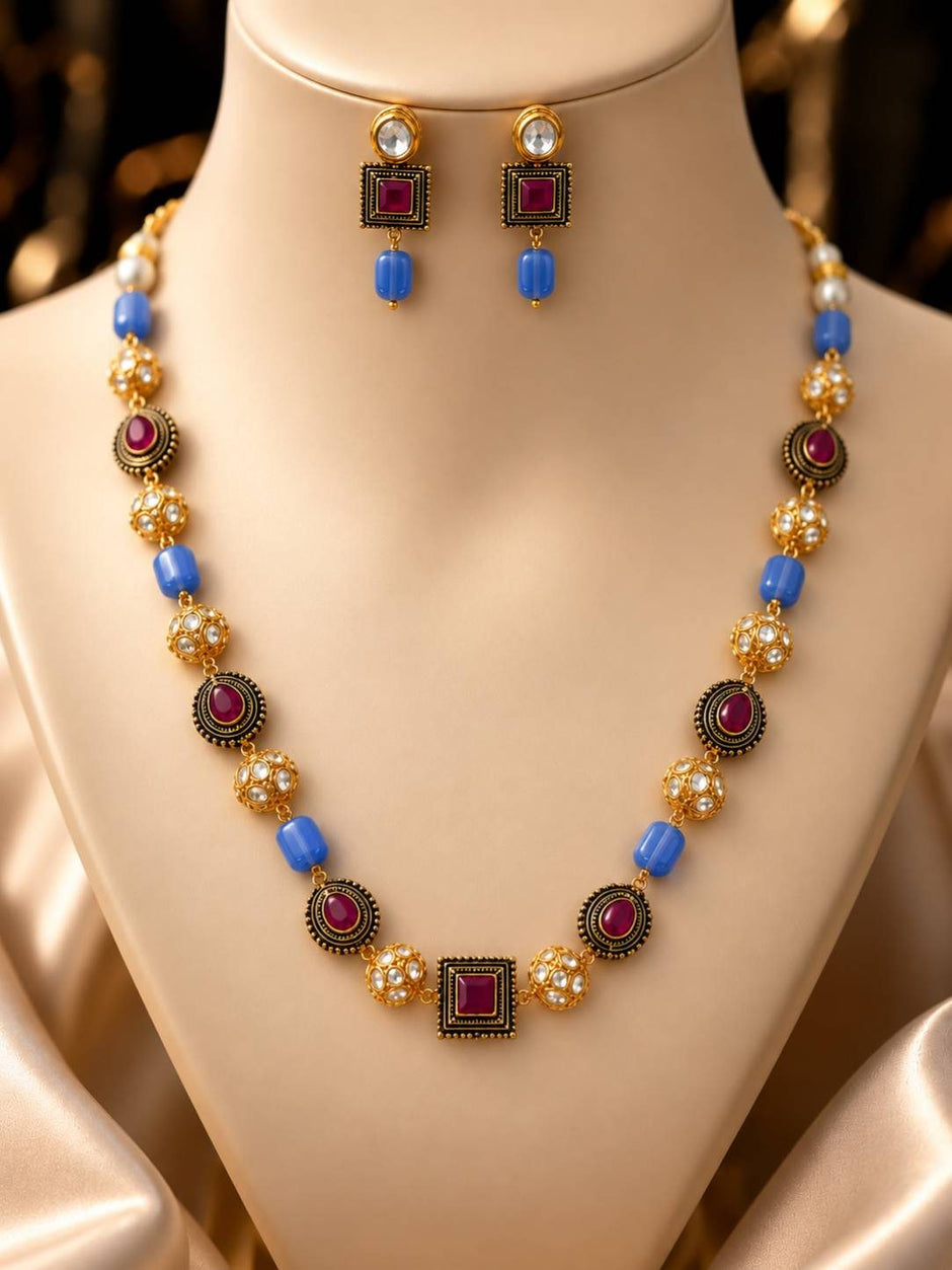 Gold-plated kundan beaded necklace set with blue barrel beads and square pendant displayed on a cream jewellery bust with matching earrings