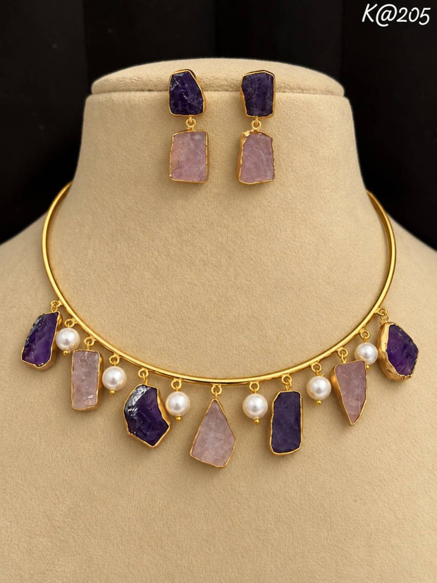 Gold-plated choker necklace and drop earrings with purple and pink raw stones and pearl accents on a beige mannequin bust