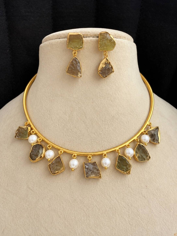Gold-plated raw stone choker necklace set with olive-green stones and white faux pearls displayed on a cream jewellery bust