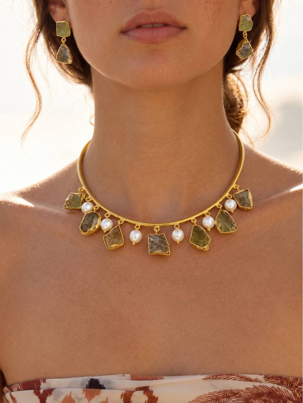 Model wearing gold-plated raw stone choker necklace and matching drop earrings with a strapless printed top outdoors