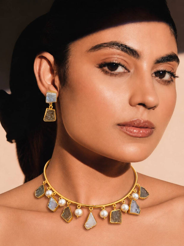 Model wearing gold-plated stone choker necklace and matching two-tier drop earrings against a warm beige background