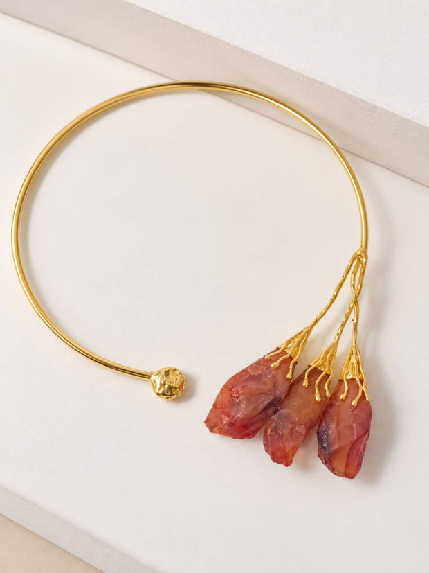 Gold-plated open choker collar with three rough red-orange stones on a white surface