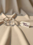 Clear acrylic cuff bangle with faceted detailing resting on cream draped fabric with The Glam Pouch tag