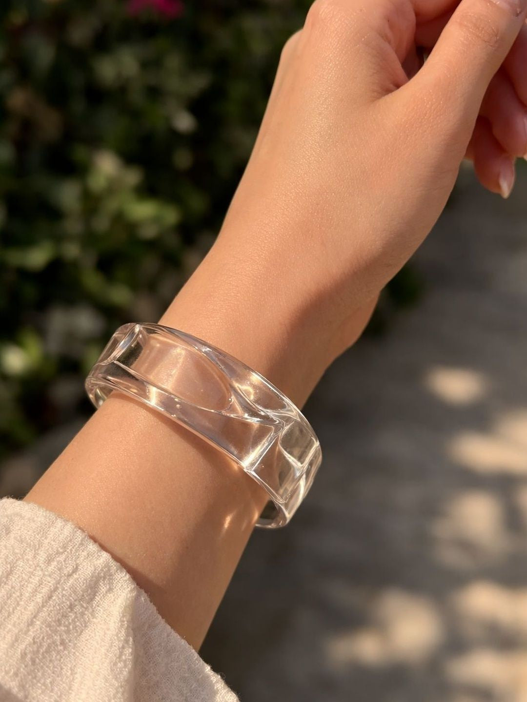 Clear acrylic cuff bangle worn on a woman's wrist against a natural outdoor background