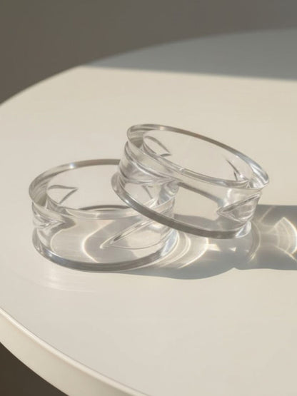 Two clear geometric acrylic bangles resting on a white surface in natural sunlight
