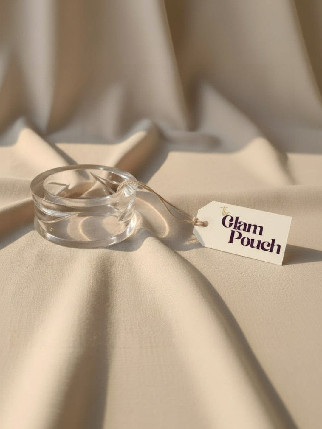 Single clear acrylic bangle on beige fabric beside a The Glam Pouch product tag