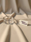 Single clear acrylic bangle on beige fabric beside a The Glam Pouch product tag