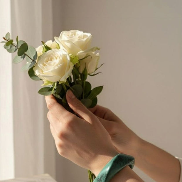 Hands holding white roses wearing a chunky green marble-finish resin bangle on the wrist