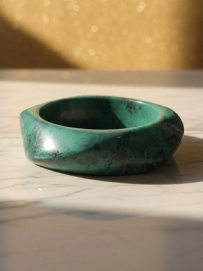 Chunky green marble resin bangle lying flat on a white marble surface in warm sunlight