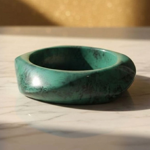 Chunky green marble resin bangle lying flat on a white marble surface in warm sunlight