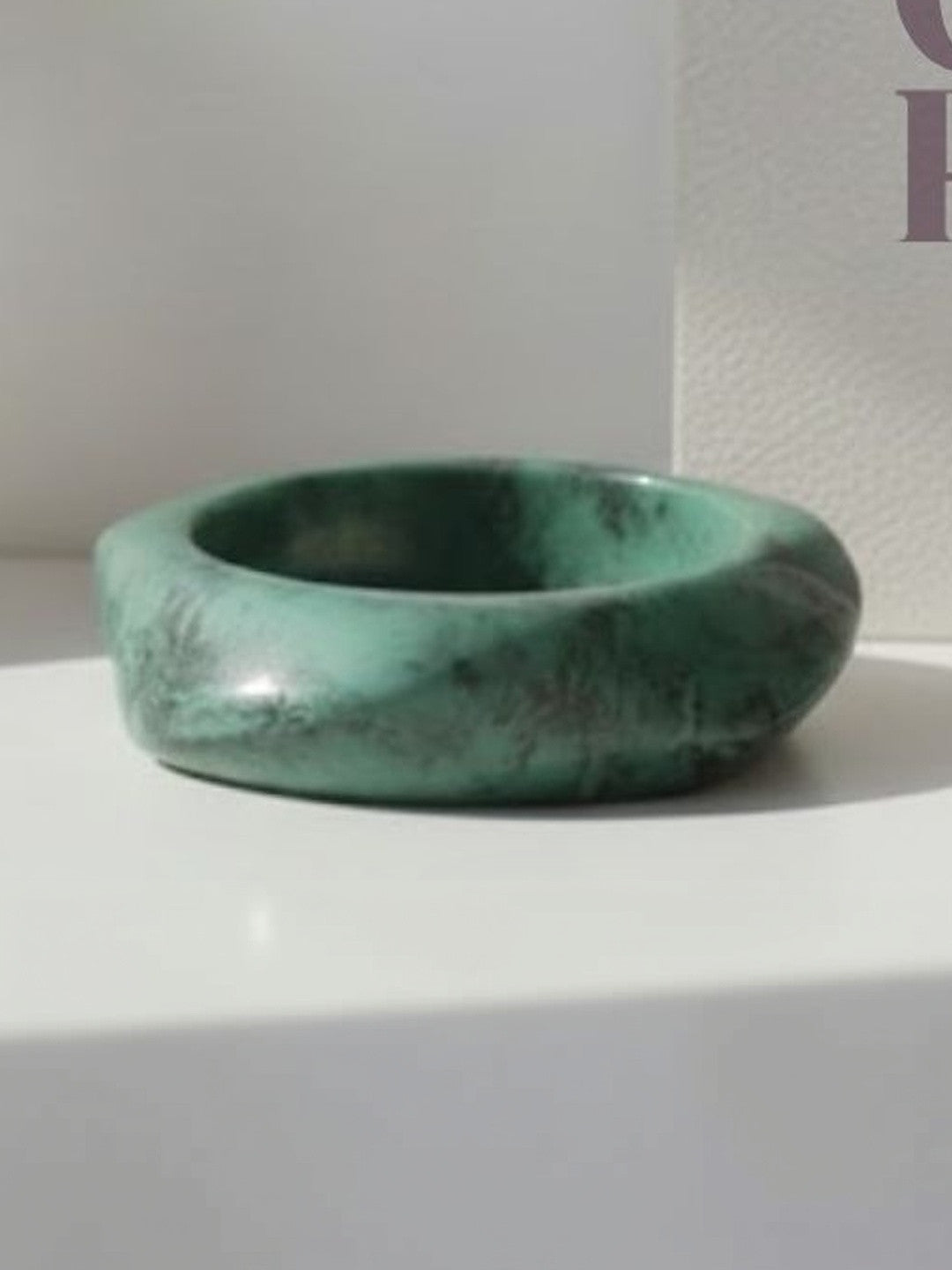 Side view of a high-gloss green marble resin bangle on a white surface beside a book