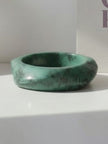 Side view of a high-gloss green marble resin bangle on a white surface beside a book
